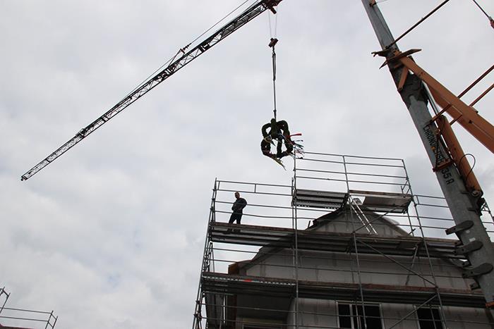 Der Richtkranzschwebt über das Dach. Ein Zimmermann ist bereit, ihn zu befestigen.