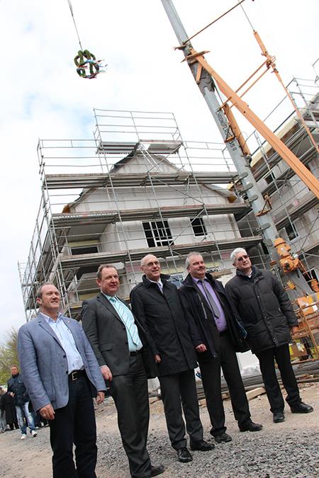 Die Verantwortlichen der Caritas stehen dem Gebäude, auf das der Richtkranz gehoben wird.