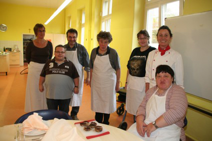 Alle Teilnehmer und Begleiter des Kochkurses haben sich im Halbkreis in der Lernküche zu einem Gruppenfoto aufgestellt. 